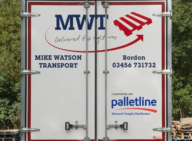 Rear doors of a Mike Watson Transport (MWT) lorry, displaying company branding with the slogan ‘Delivered the right way,’ contact number, and partnership logo for Palletline – Network Freight Distribution