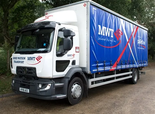MWT-branded delivery lorry with blue Palletline curtain side, parked on a concrete surface beside trees. Logos read ‘Mike Watson Transport’ and ‘Delivered the right way.